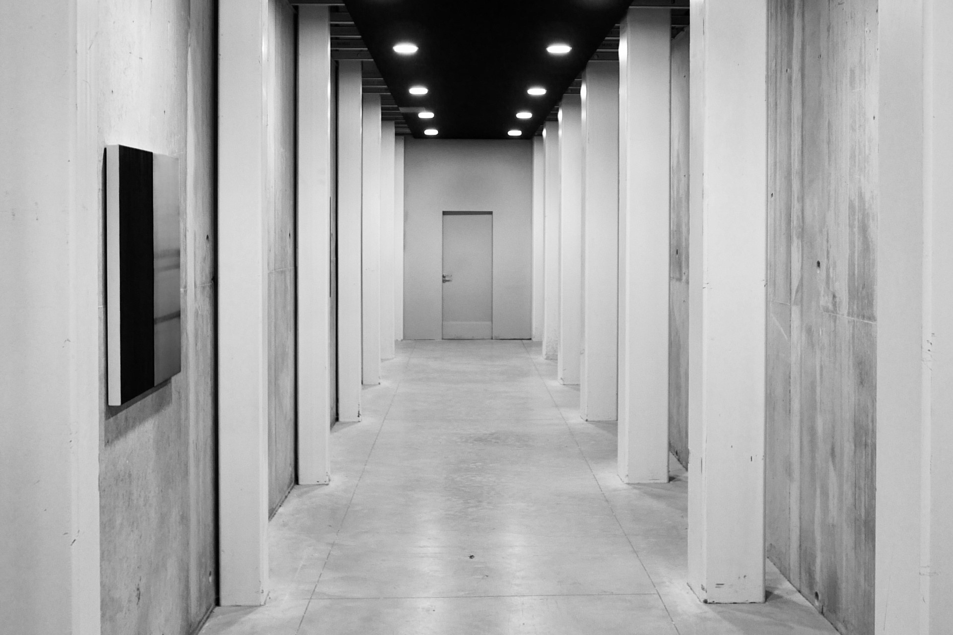 Moderní kancelářská chodba s betonovými sloupy a černým stropem, vhodná pro firmy s ISO certifikací a compliance služby.